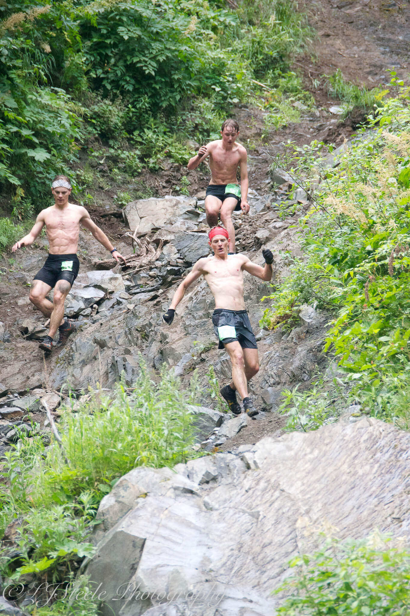 Three men running down rocky hillside.